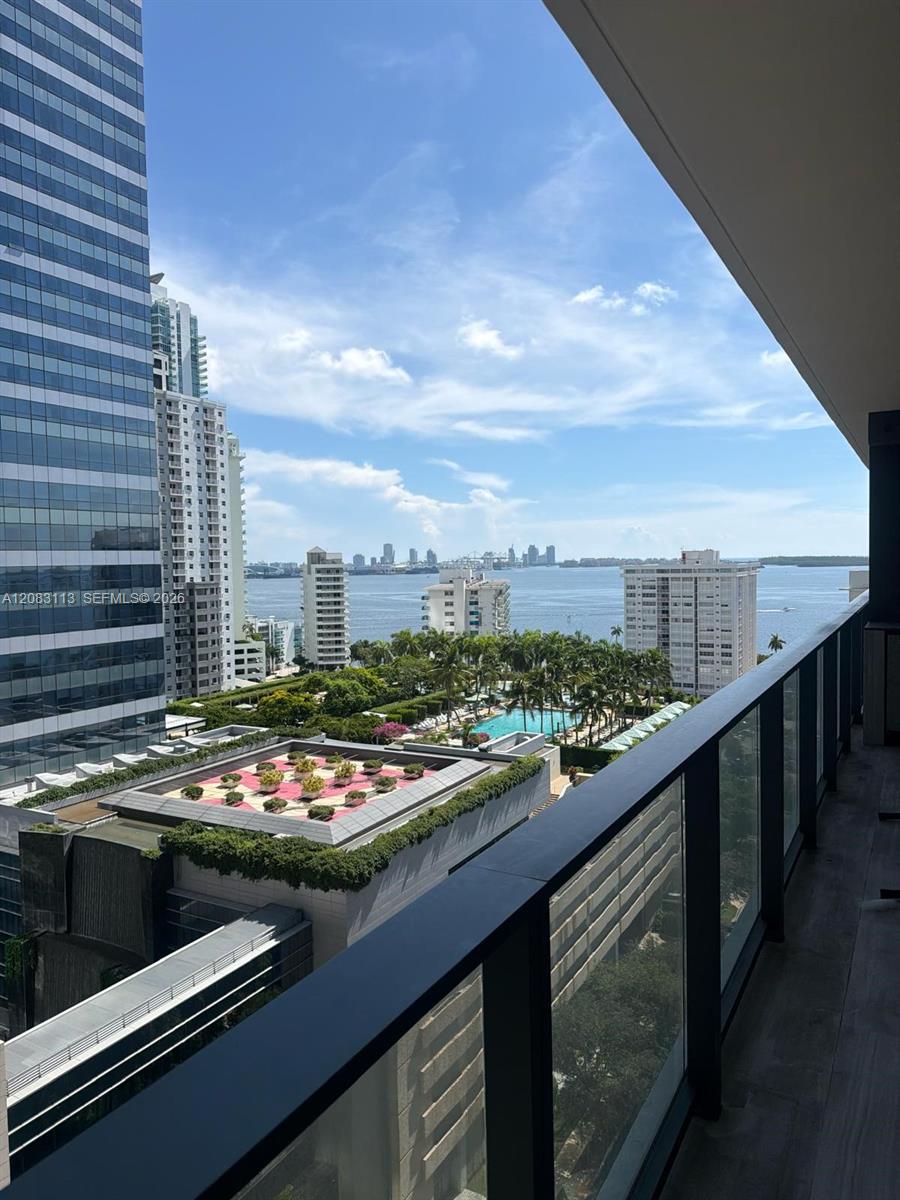High-rise condo balcony overlooking the bay, distant skyline, and landscaped pool deck.