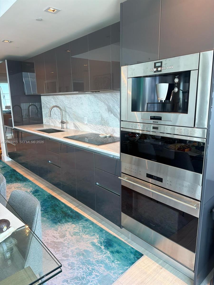 Modern kitchen with glossy dark cabinetry, built-in stainless appliances, and a turquoise patterned floor runner.