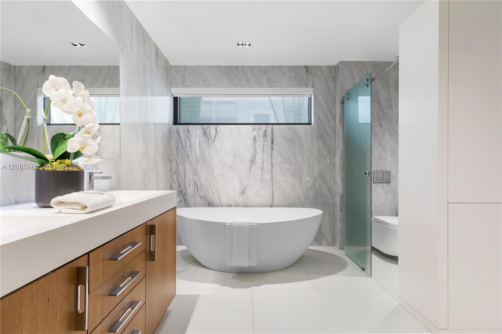 Modern marble bathroom with a freestanding soaking tub, glass shower screen, and wood vanity.