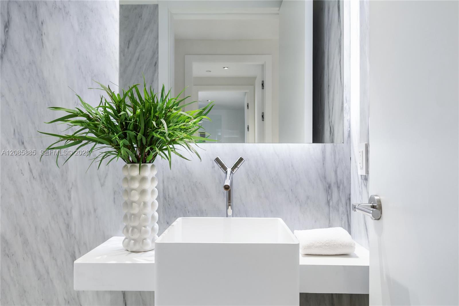 Modern bathroom vanity with a rectangular vessel sink, marble walls, chrome faucet, and leafy plant.