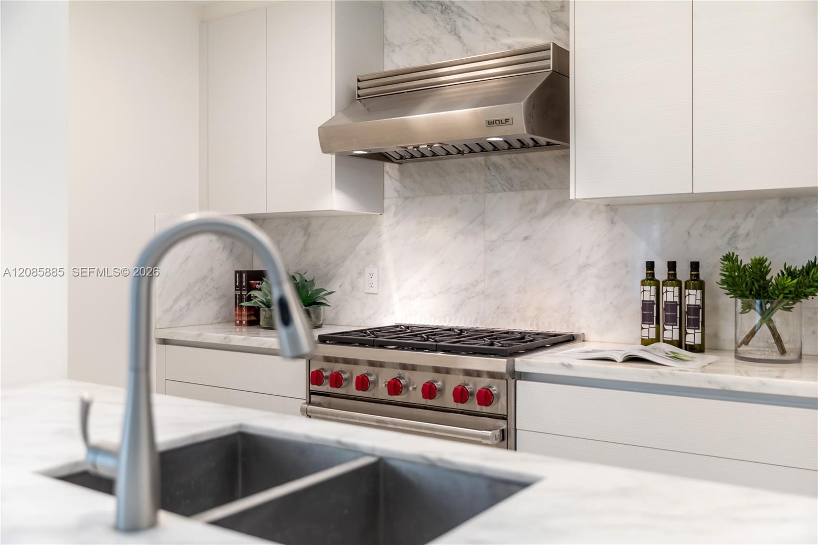 Modern kitchen with marble counters, a stainless gas range with red knobs, and a deep double-basin sink.