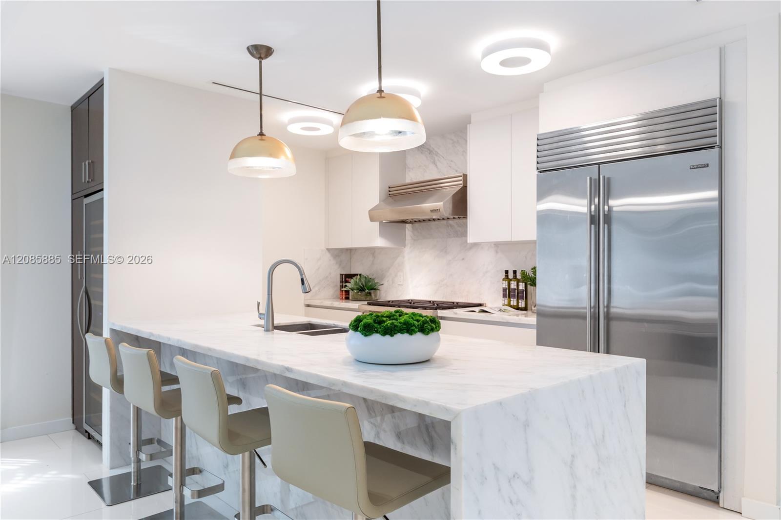 Modern kitchen with a marble waterfall island, bar stools, and stainless steel appliances.
