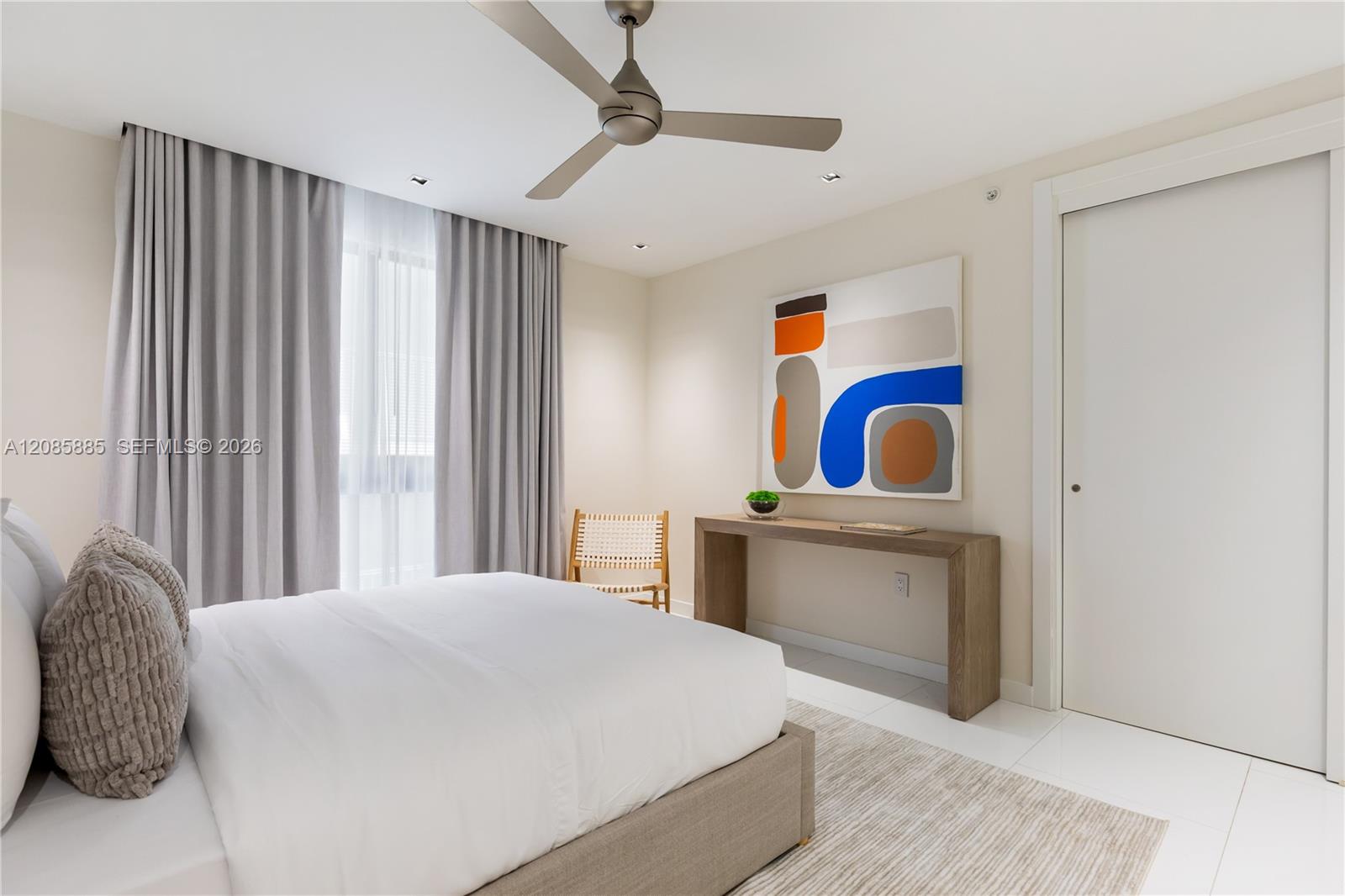Furnished bedroom with gray curtains, a ceiling fan, and colorful abstract wall art.
