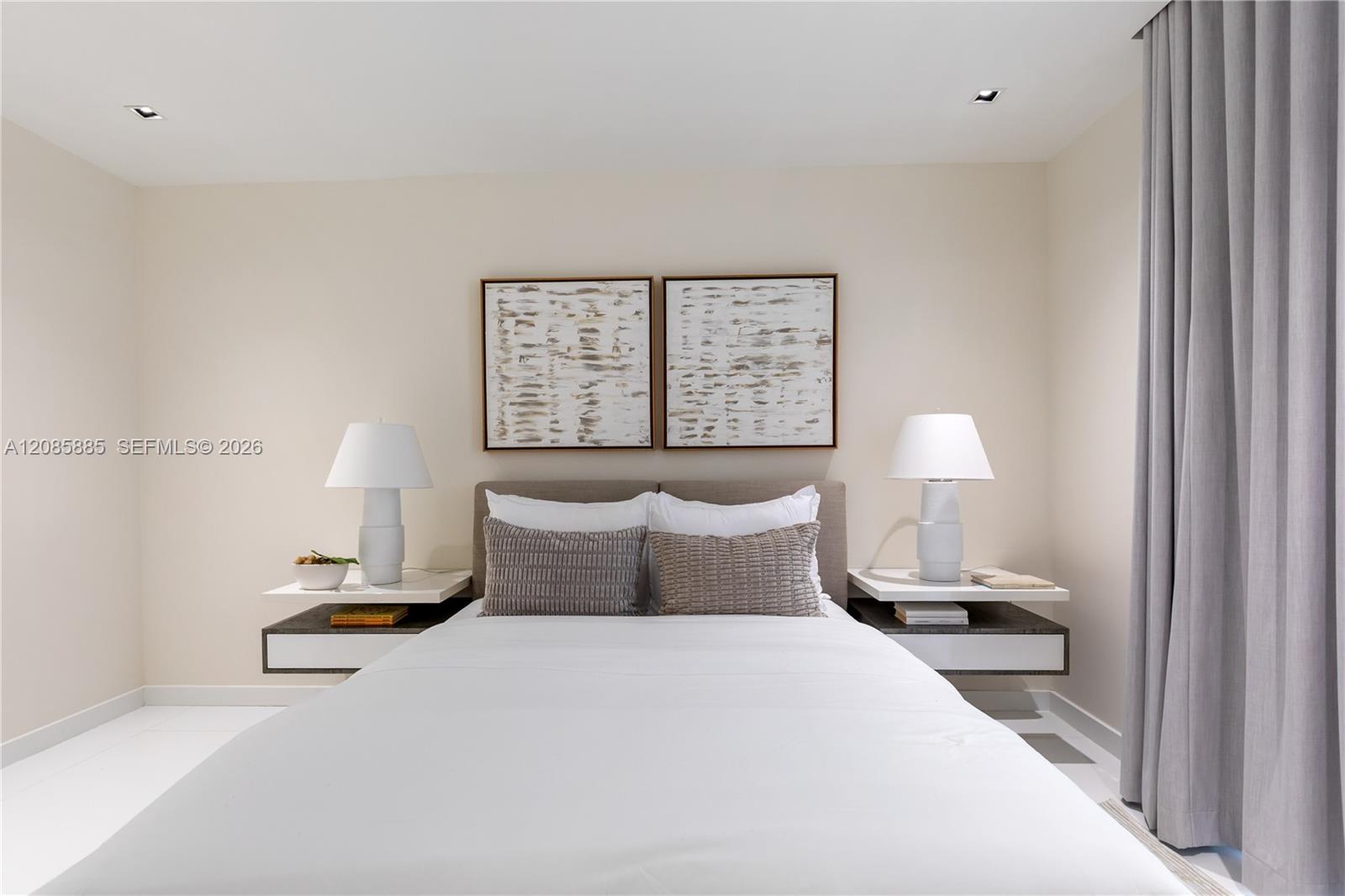 Staged bedroom with a white bed, twin abstract prints, and gray floor-length curtains.