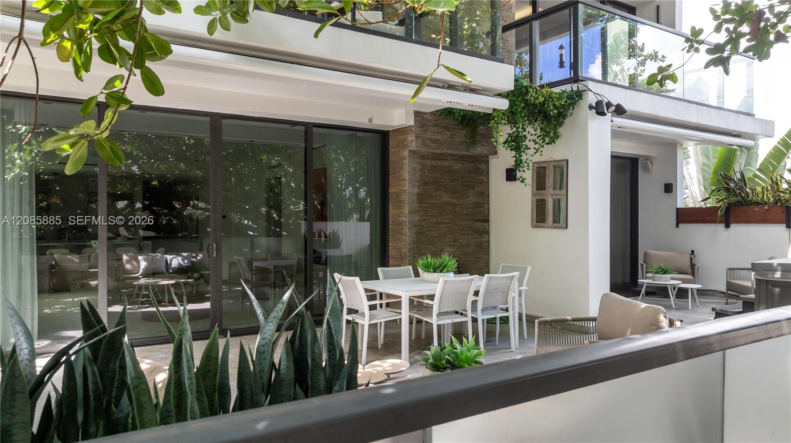 Modern residence patio with outdoor dining furniture, lounge seating, and tropical plants.