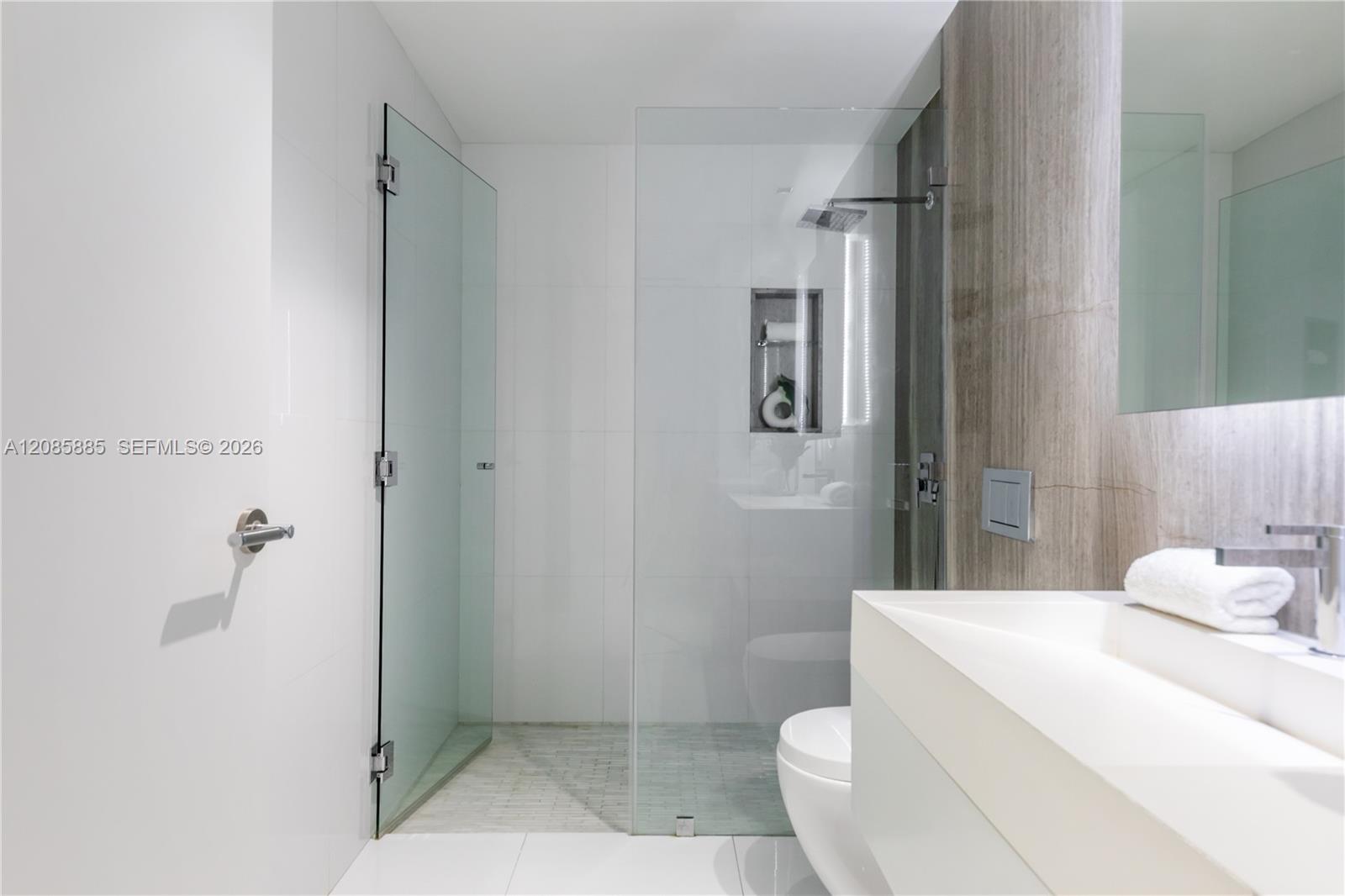 Modern bathroom with a glass walk-in shower, recessed niche, and white vanity.