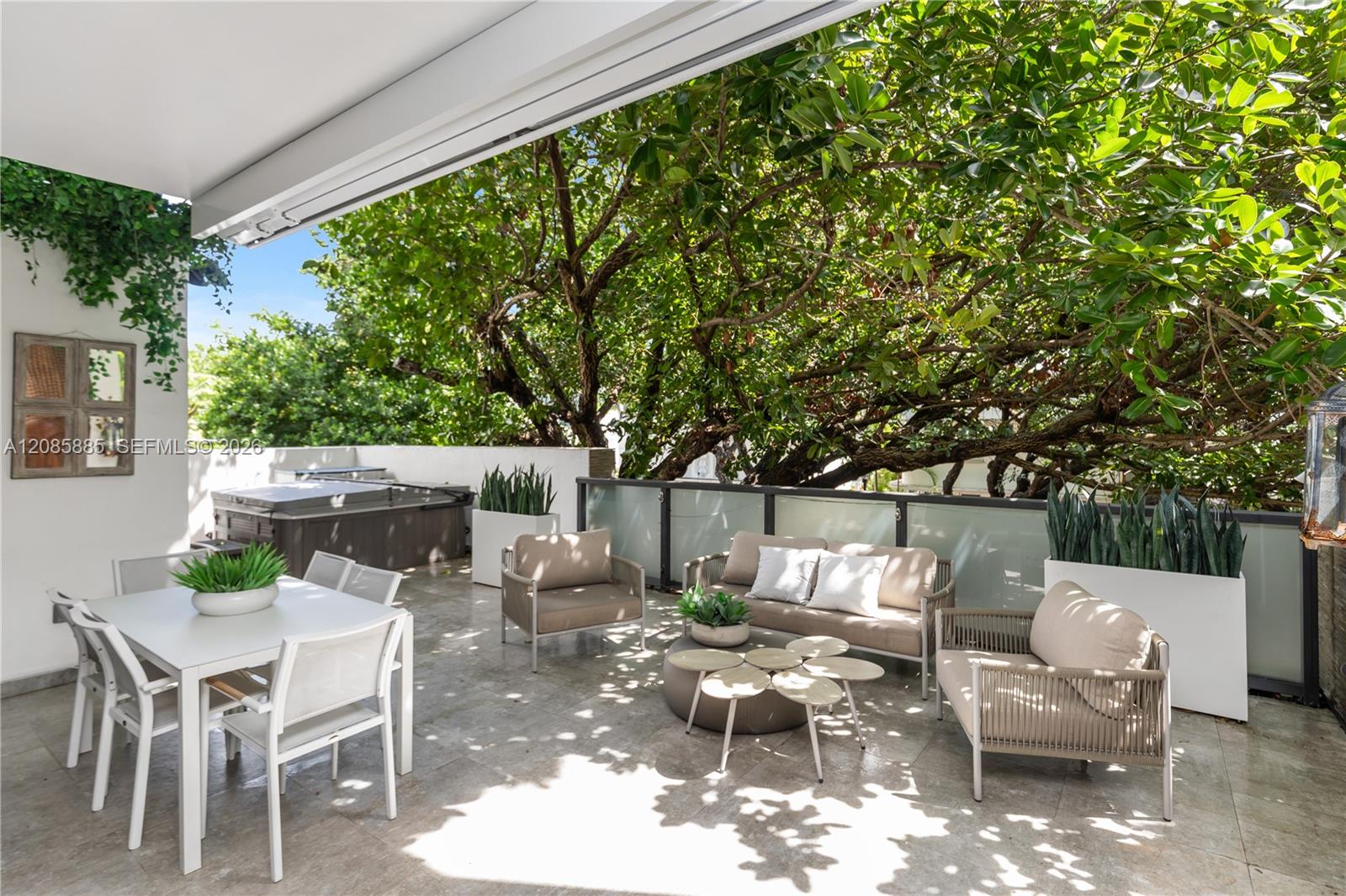 Furnished terrace with a hot tub, outdoor dining set, and lounge seating beneath a leafy tree canopy.
