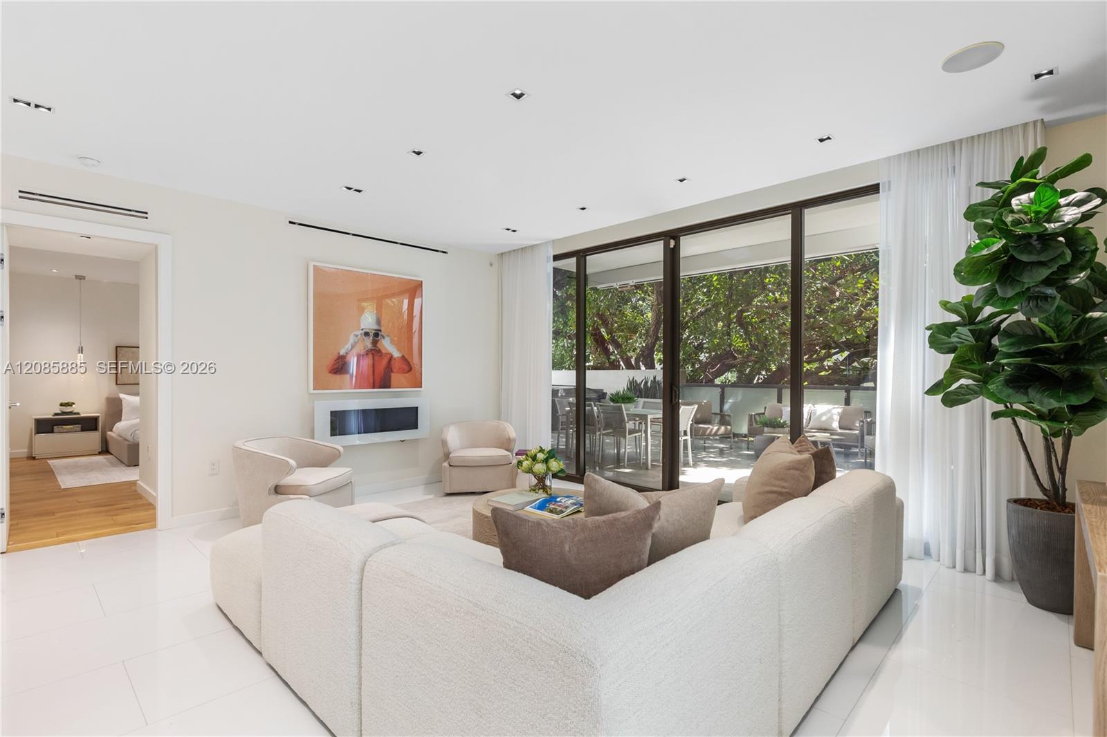 Furnished living room with a white sectional, fireplace, and glass doors opening to a leafy patio.