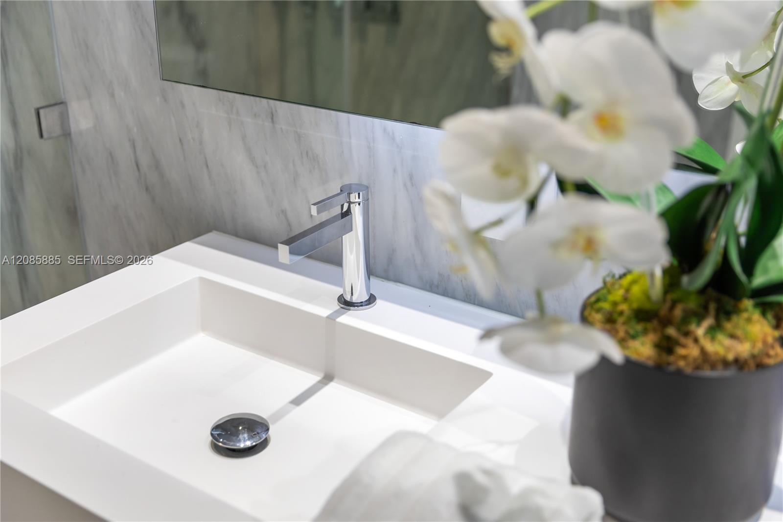 Bathroom sink with a chrome faucet, gray marble wall, and potted white orchid.