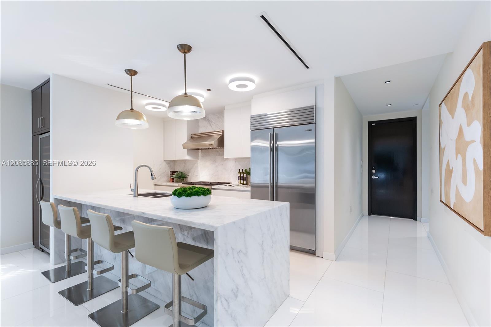 Modern white kitchen with marble island, bar seating, and stainless steel appliances.
