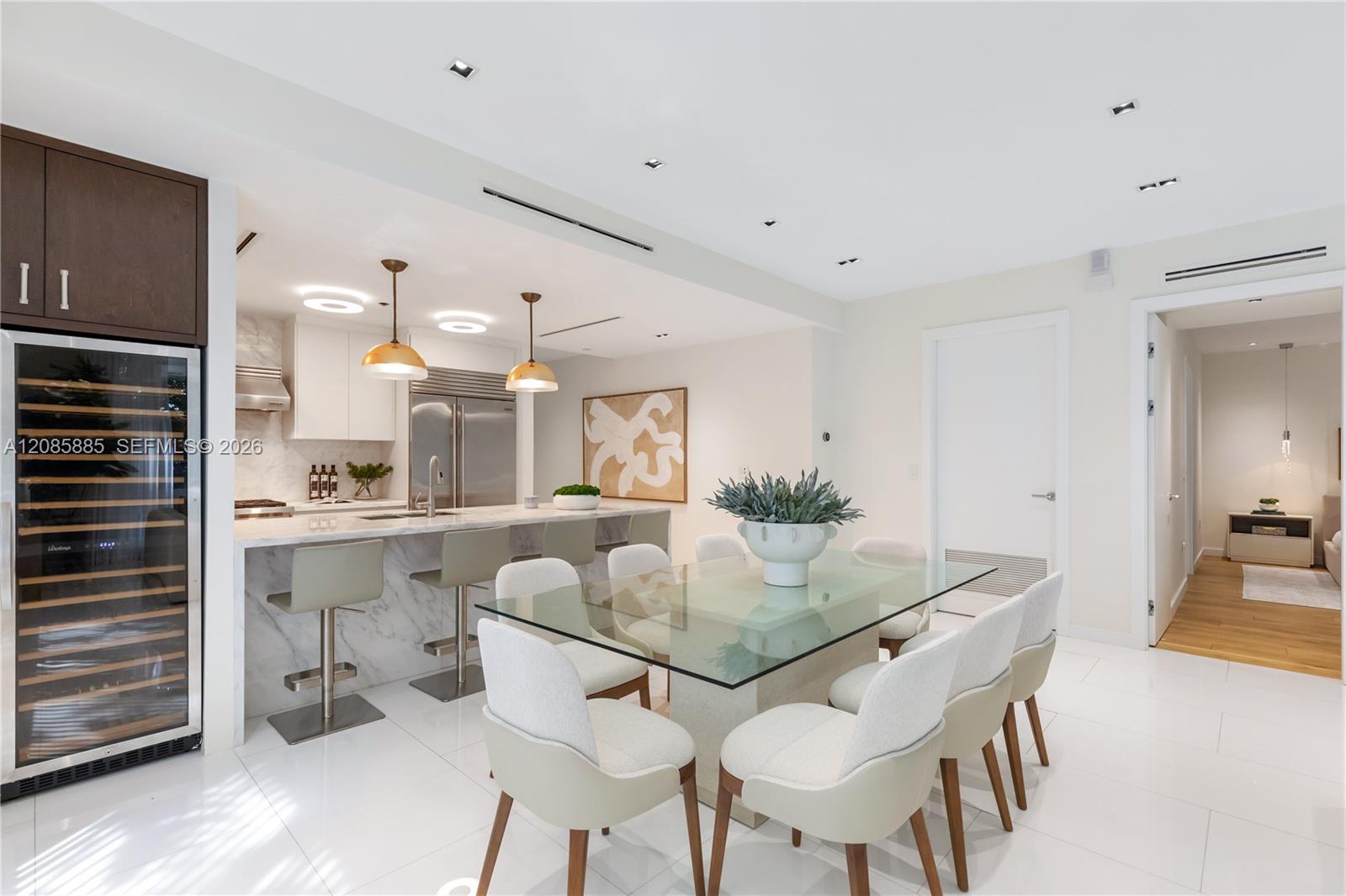 Open-plan kitchen and dining area with marble counters, glass table, and built-in wine refrigerator.