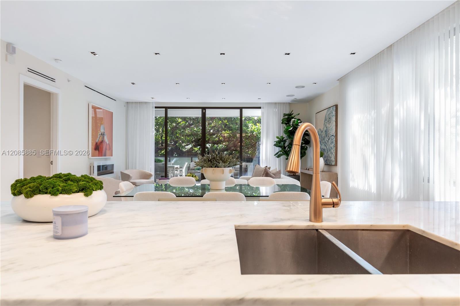 Bright kitchen with a marble island, copper faucet, and views through glass doors to a leafy patio.