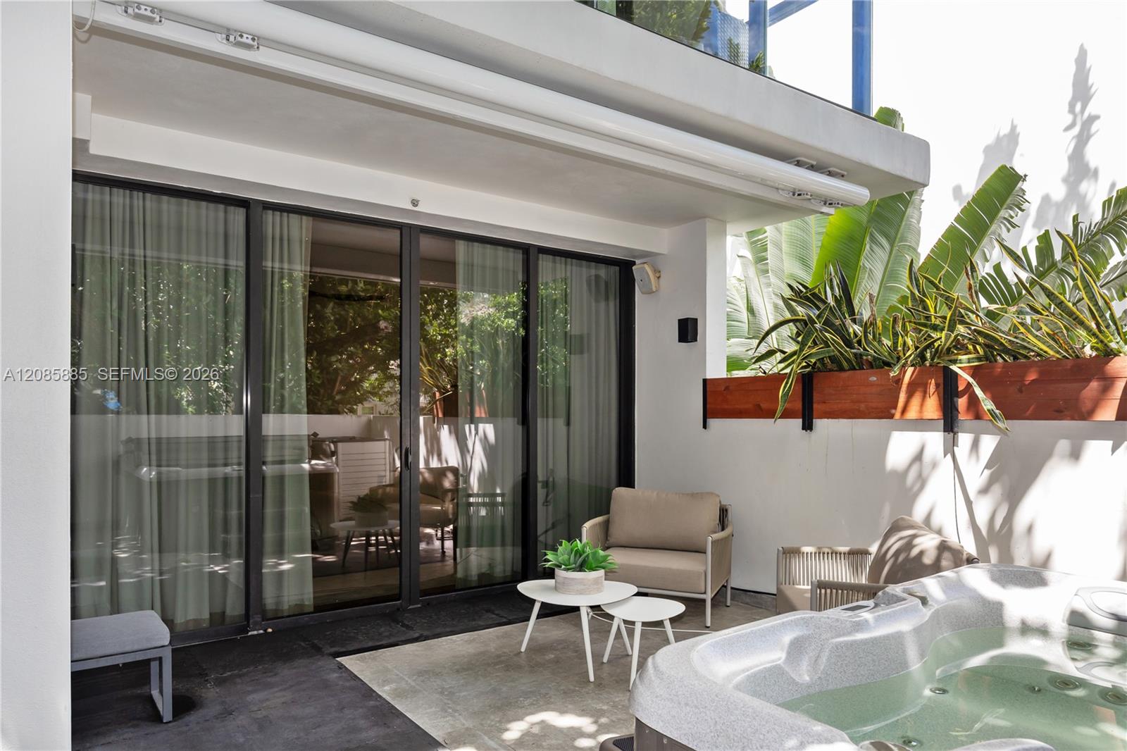 Furnished patio with a built-in hot tub, lounge seating, and tropical planters beside sliding glass doors.