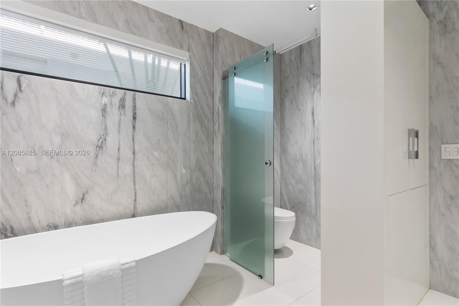 Modern marble bathroom with a freestanding tub and frosted-glass divider.