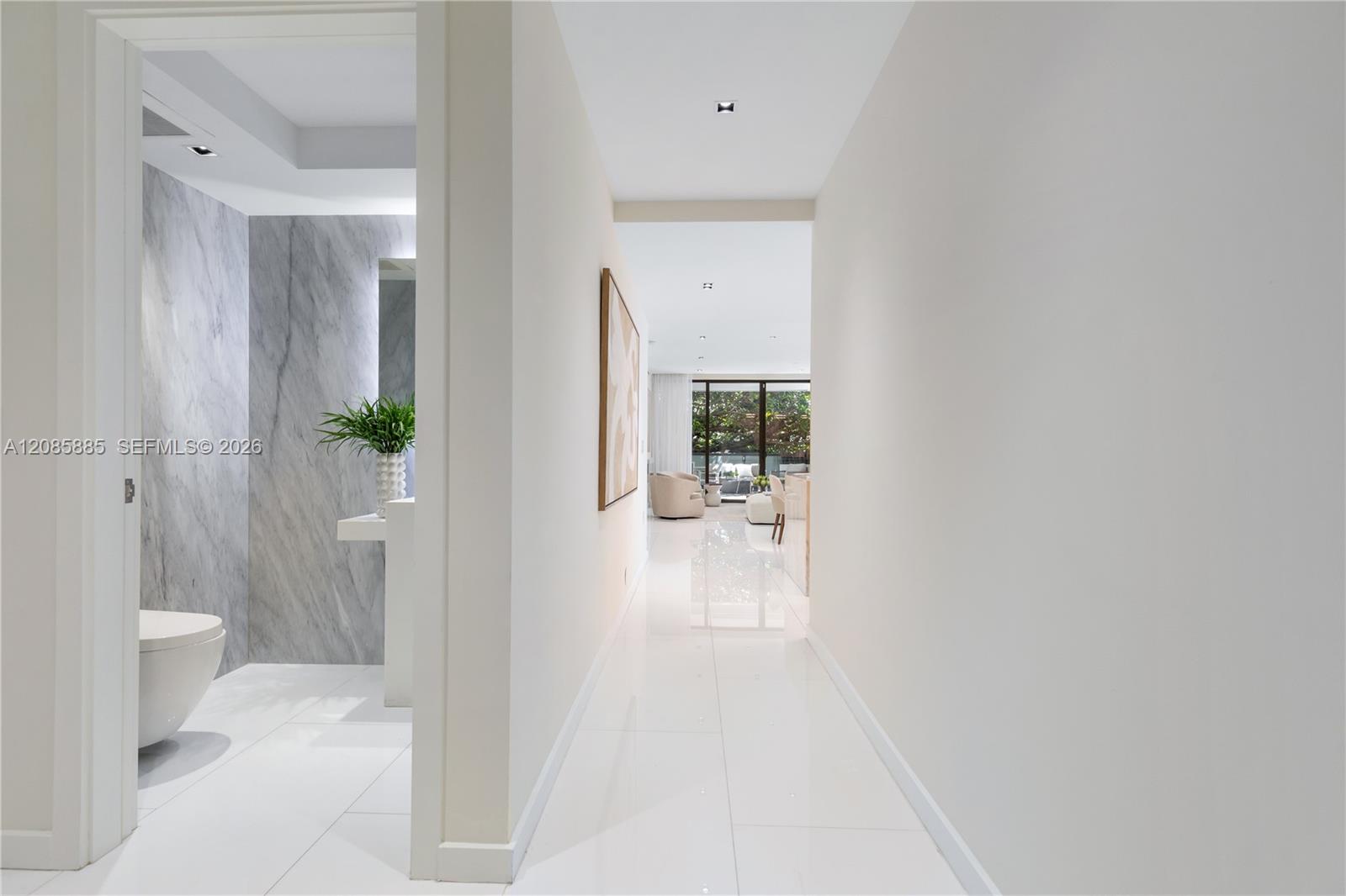 Modern condo hallway with glossy white floors, a marble bathroom, and a furnished living area beyond.