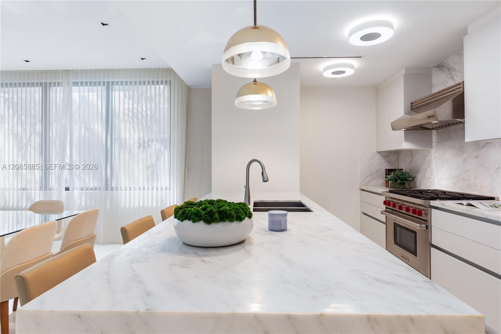 Modern kitchen with a large marble island, gold pendant lights, and beige dining chairs.