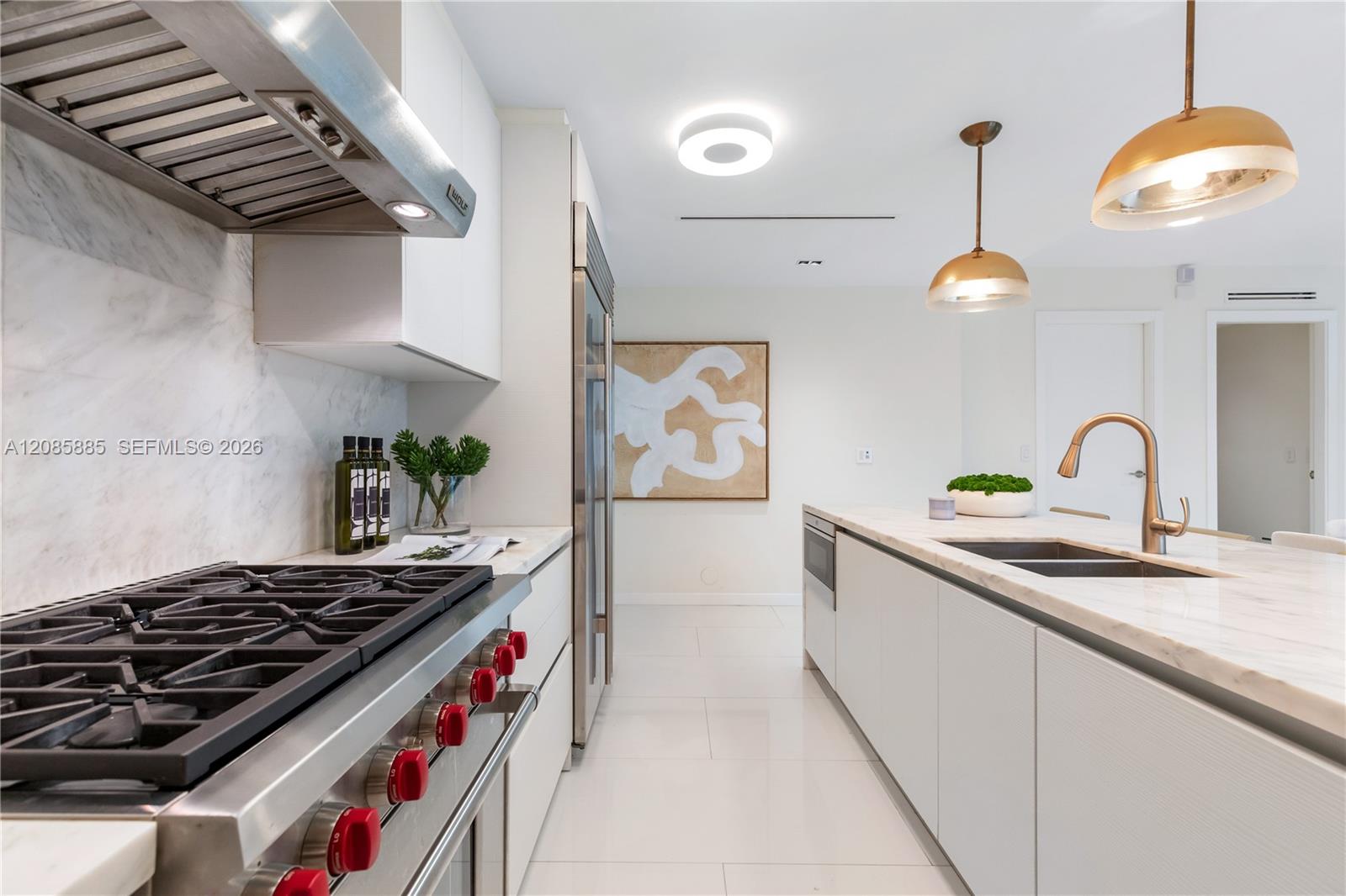 Modern white kitchen with marble island, double-basin sink, gas range, and brass pendant lights.