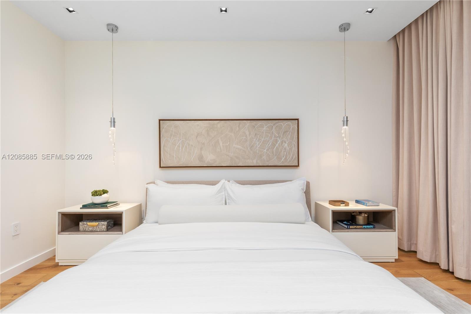 Furnished bedroom with a white bed, pendant lights, abstract artwork, and floor-length curtains.