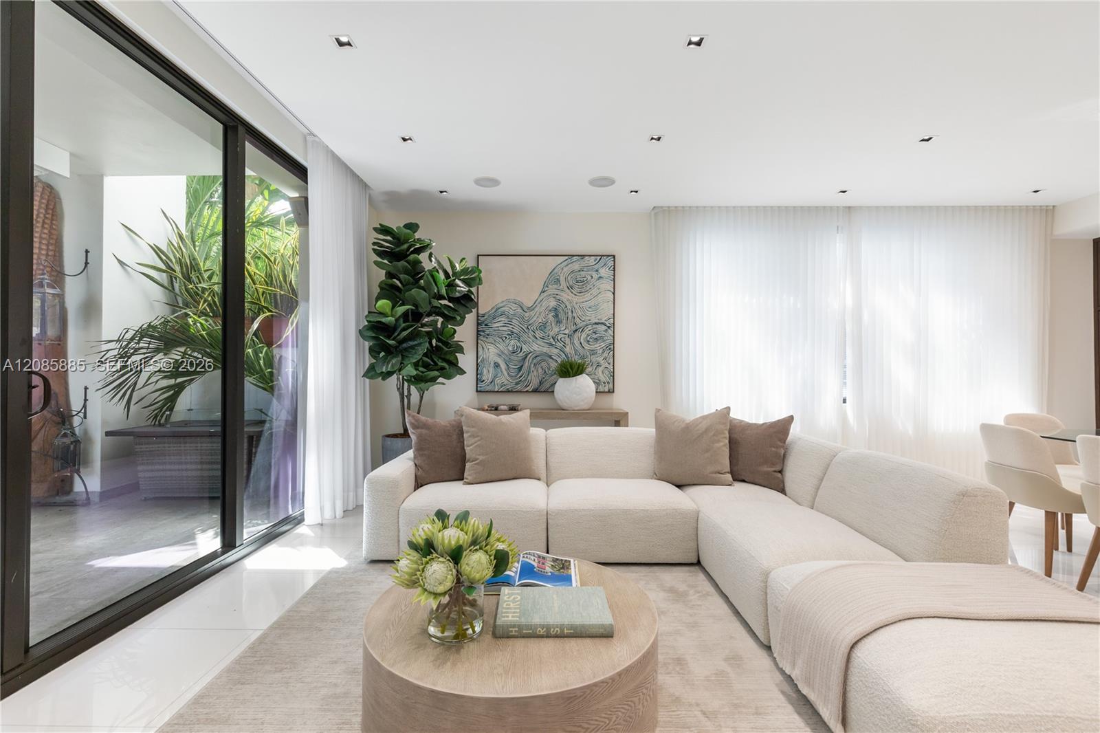 Living room with a curved cream sectional, round coffee table, and sliding doors to a leafy patio.