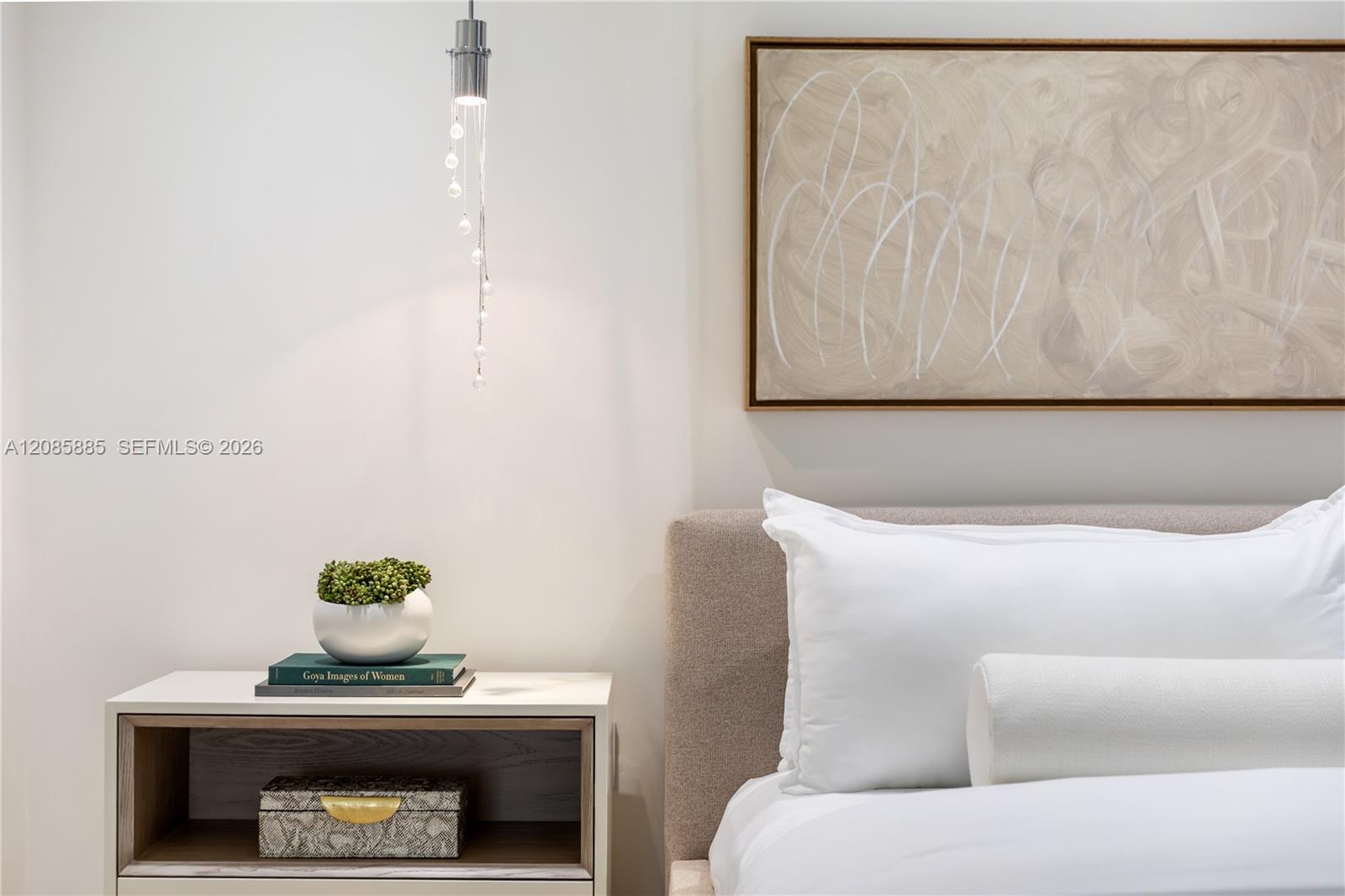 Bedroom with white bedding, an upholstered headboard, and a bedside table beneath abstract artwork.