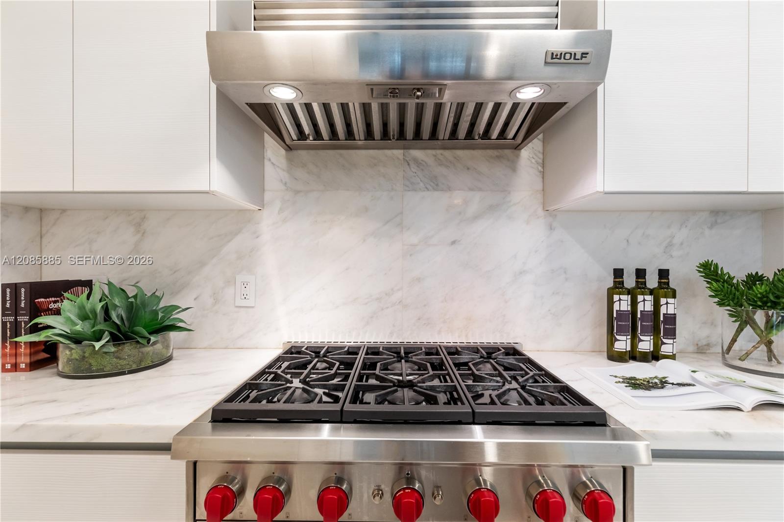 Kitchen with a stainless-steel range, oversized vent hood, and white marble backsplash.