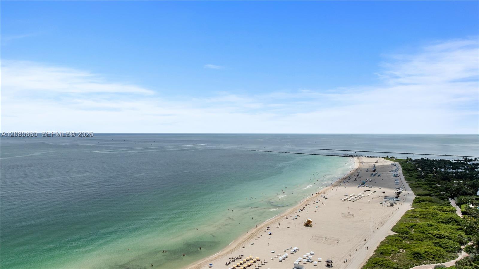 Aerial view of a sandy beach and turquoise ocean beside green coastal vegetation.