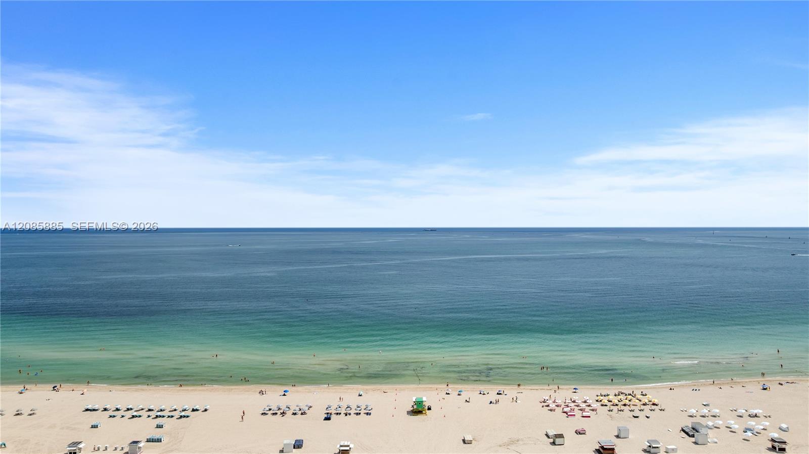 Ocean and sandy beach with rows of umbrellas viewed from above.
