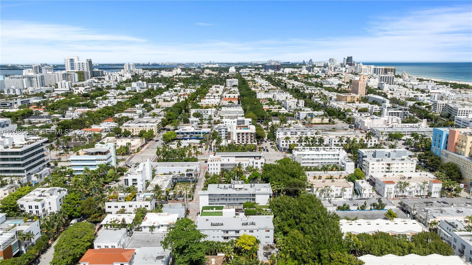 Aerial view of Miami Beach with tree-lined streets, a distant skyline, and ocean.