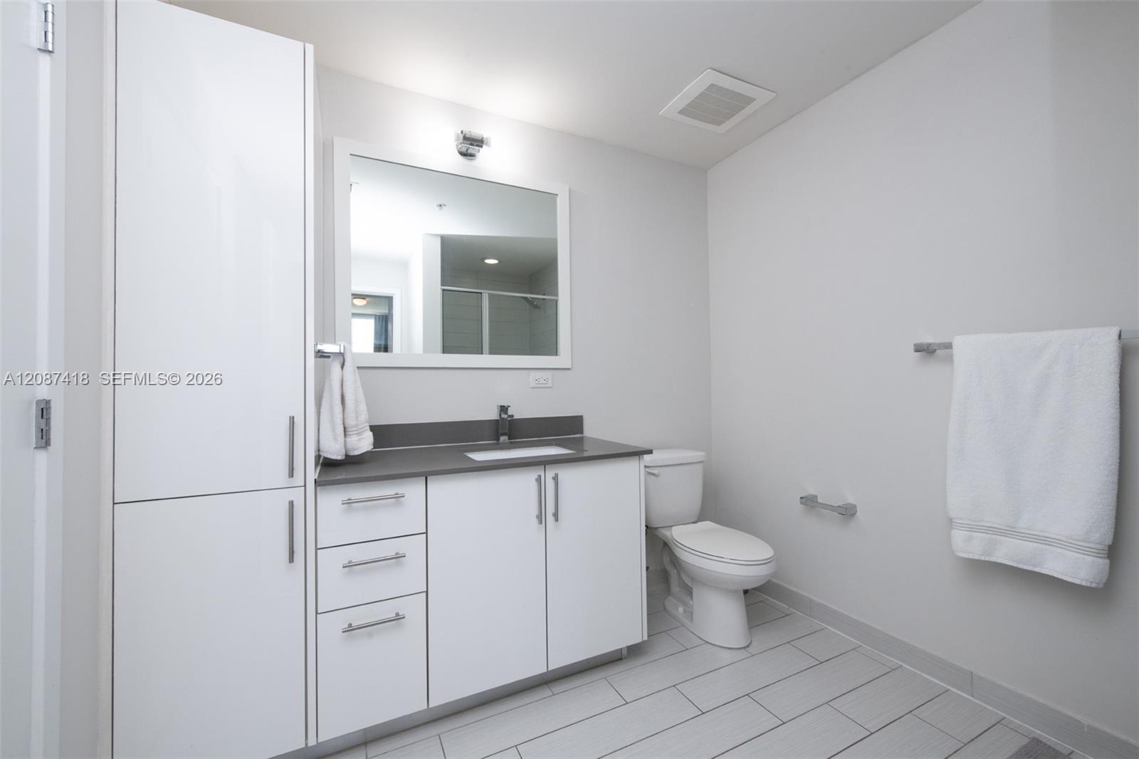 Modern bathroom with a wide white vanity, gray countertop, large mirror, and tiled floor.