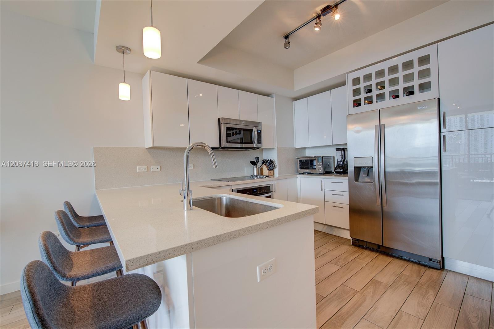 Modern condo kitchen with a white peninsula, gray stools, stainless-steel appliances, and built-in wine rack.