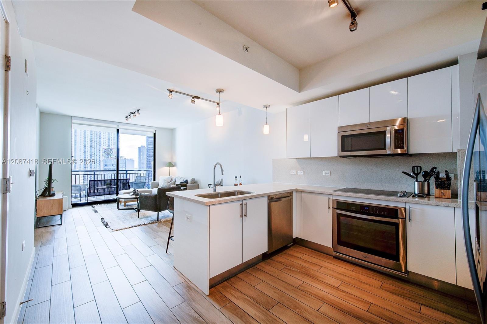 Open-plan condo kitchen with a large island, stainless steel appliances, and balcony doors overlooking the city.