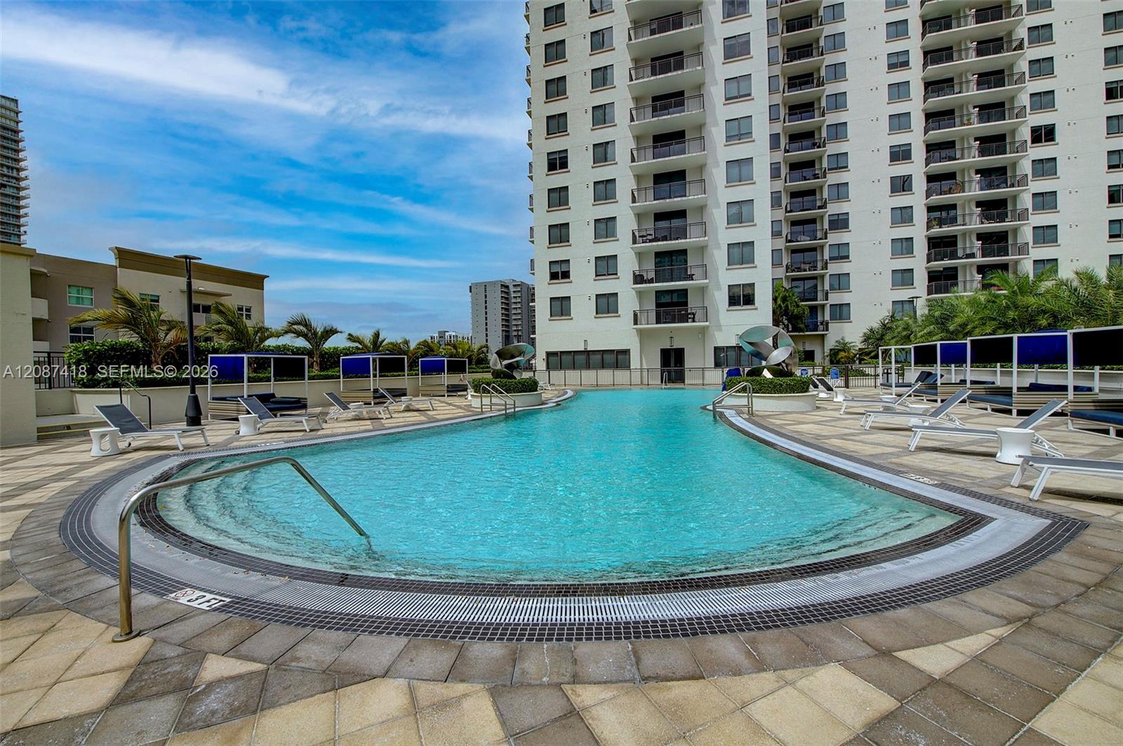 Condominium pool with curved turquoise water, sun loungers, and the high-rise building behind it.
