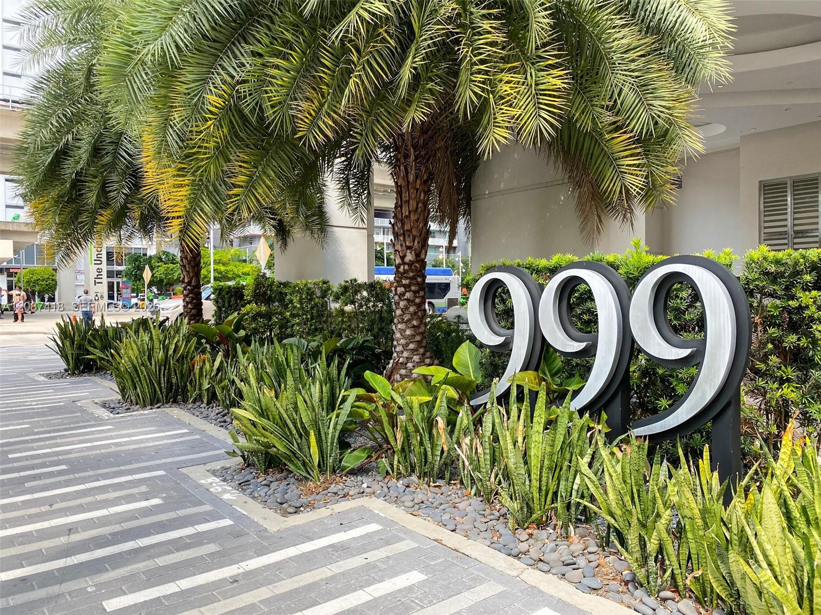 Building entrance marked 999, framed by palm trees and tropical landscaping.
