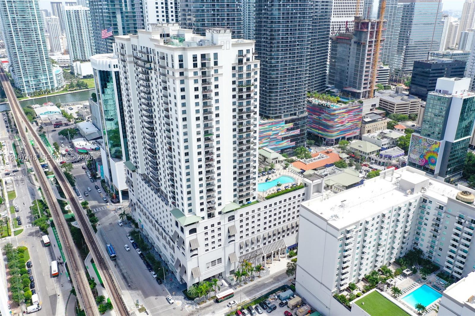 Aerial view of Brickell high-rises, rooftop pools, rail tracks, and a colorful striped building.