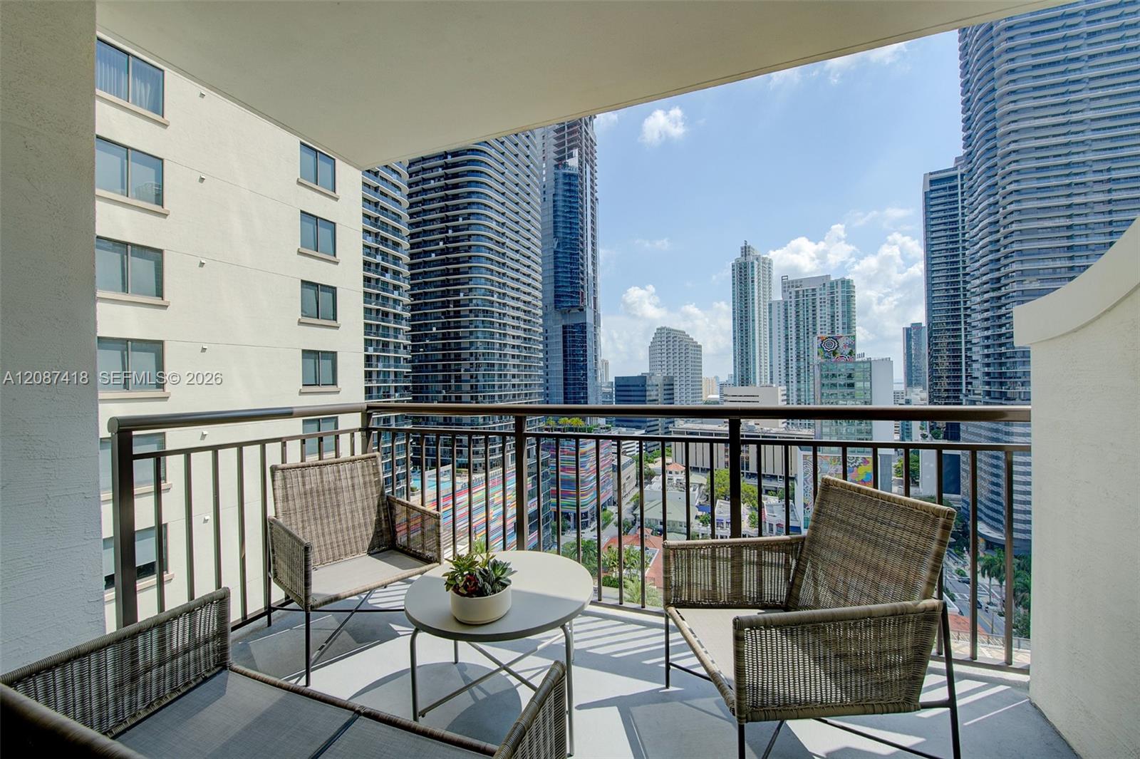 Furnished balcony with wicker seating overlooking Miami high-rises.