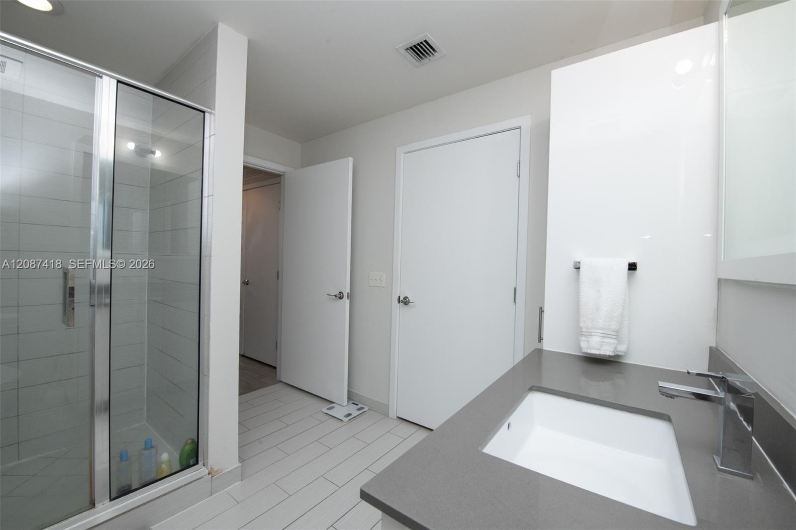Modern bathroom with a glass shower and gray vanity countertop with a rectangular sink.
