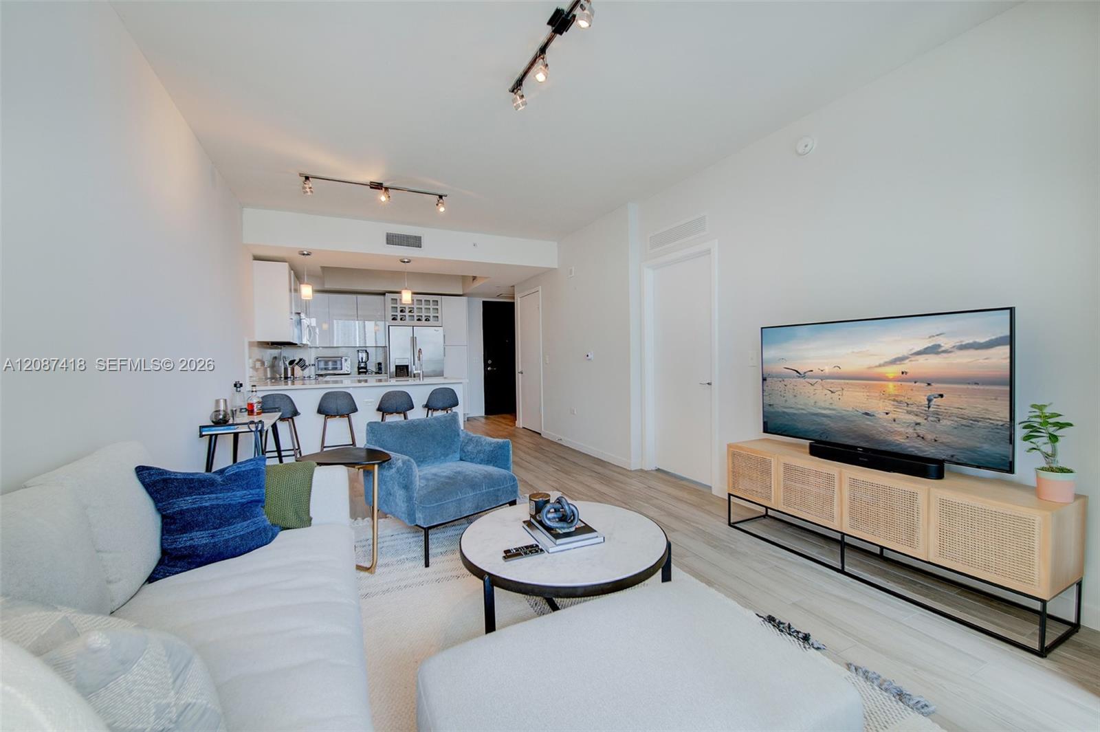 Open-plan living room with a white sofa, blue chair, and kitchen breakfast bar.