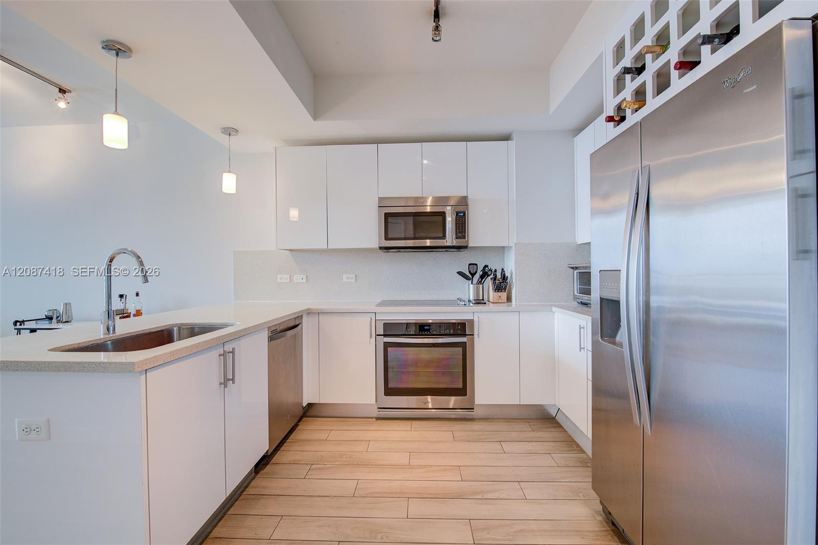 Modern white kitchen with stainless steel appliances, a breakfast counter, and a built-in wine rack.