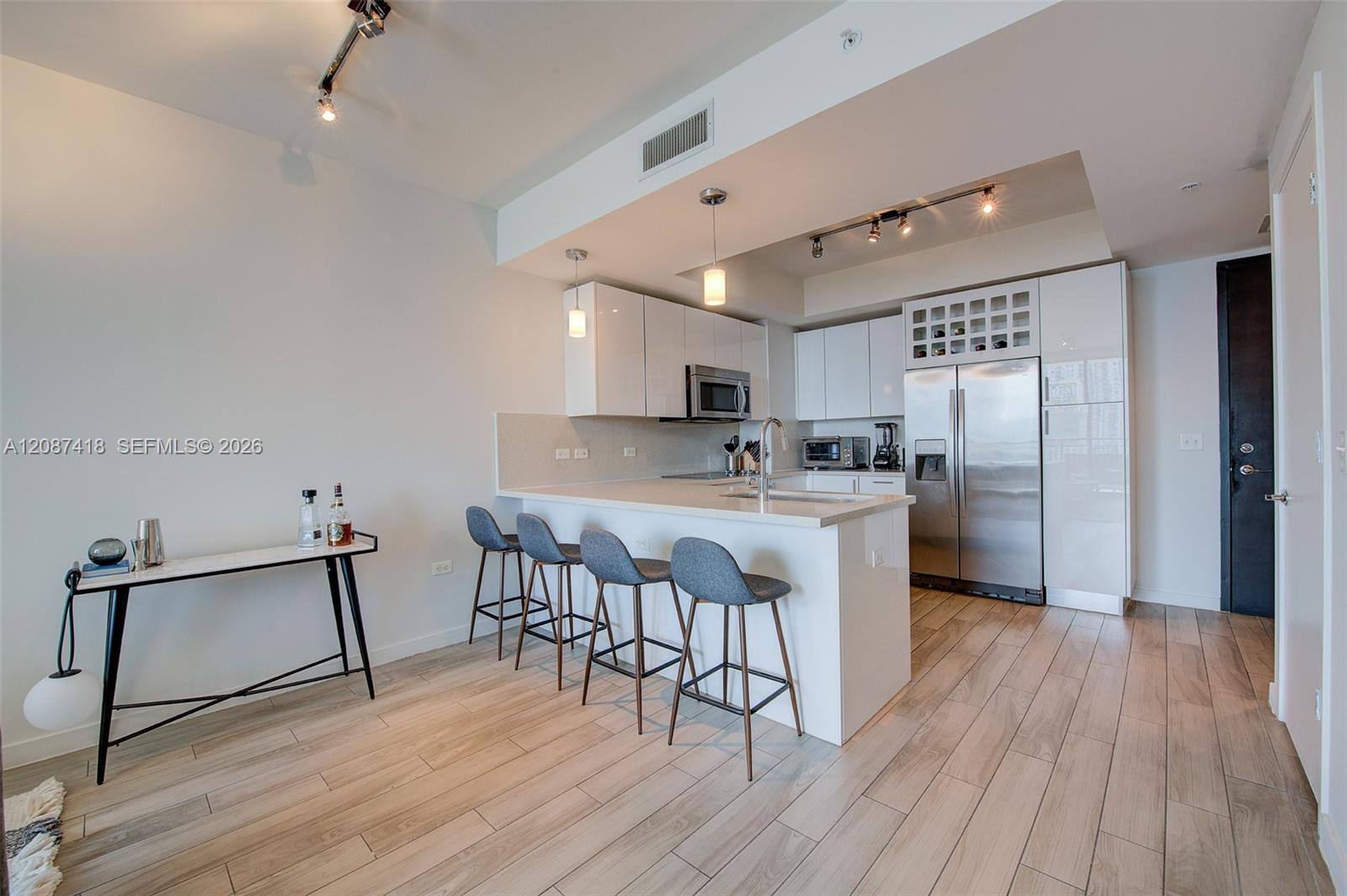 Open condo kitchen with a white island, four bar stools, and stainless steel appliances.