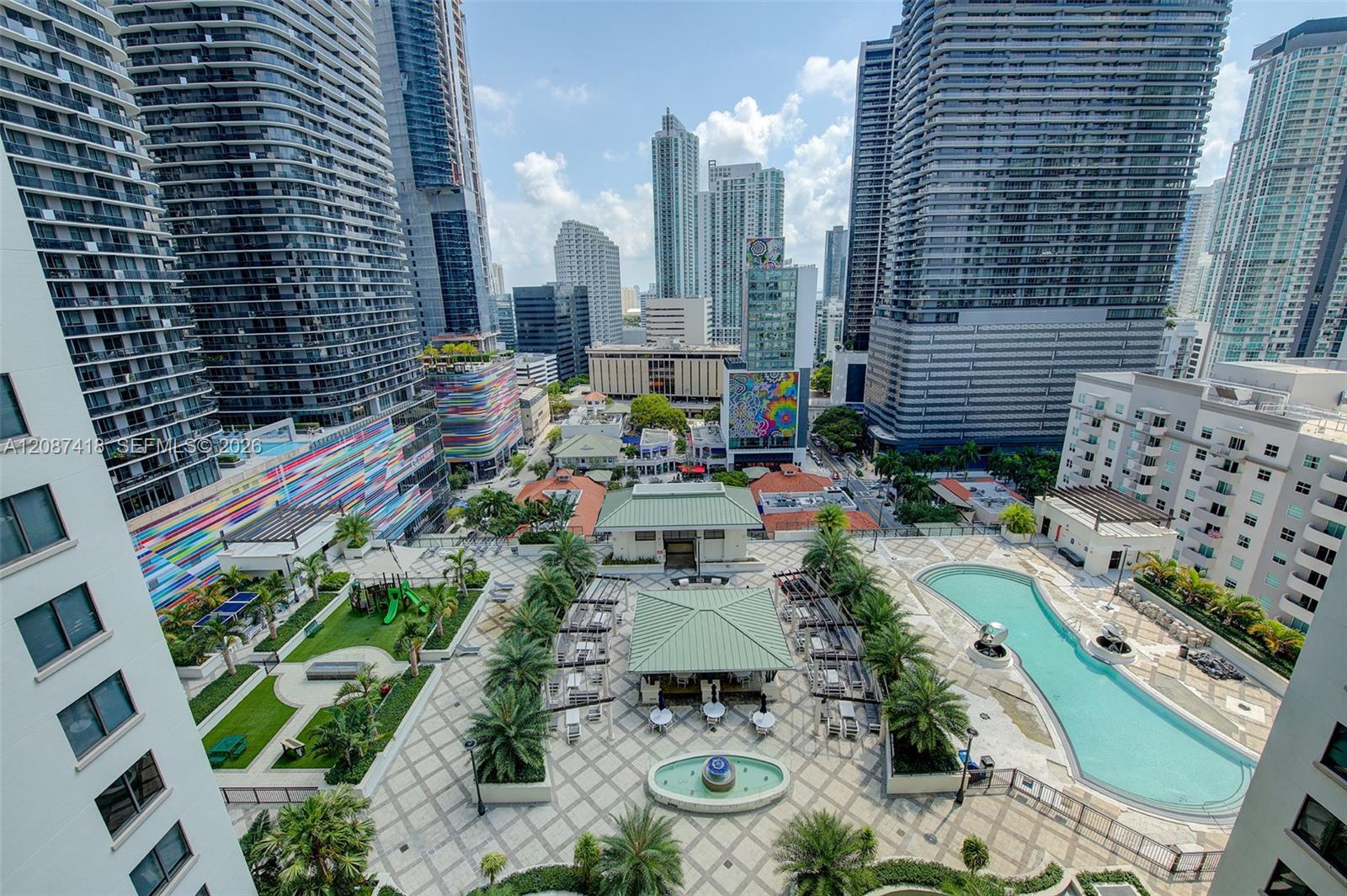 High-rise courtyard with a turquoise pool, tiled terraces, palm trees, and Miami towers.