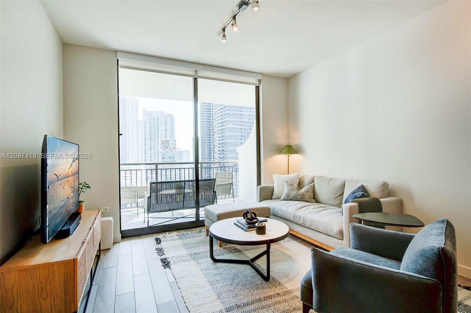 Furnished condo living room with a sectional sofa and balcony overlooking the city.