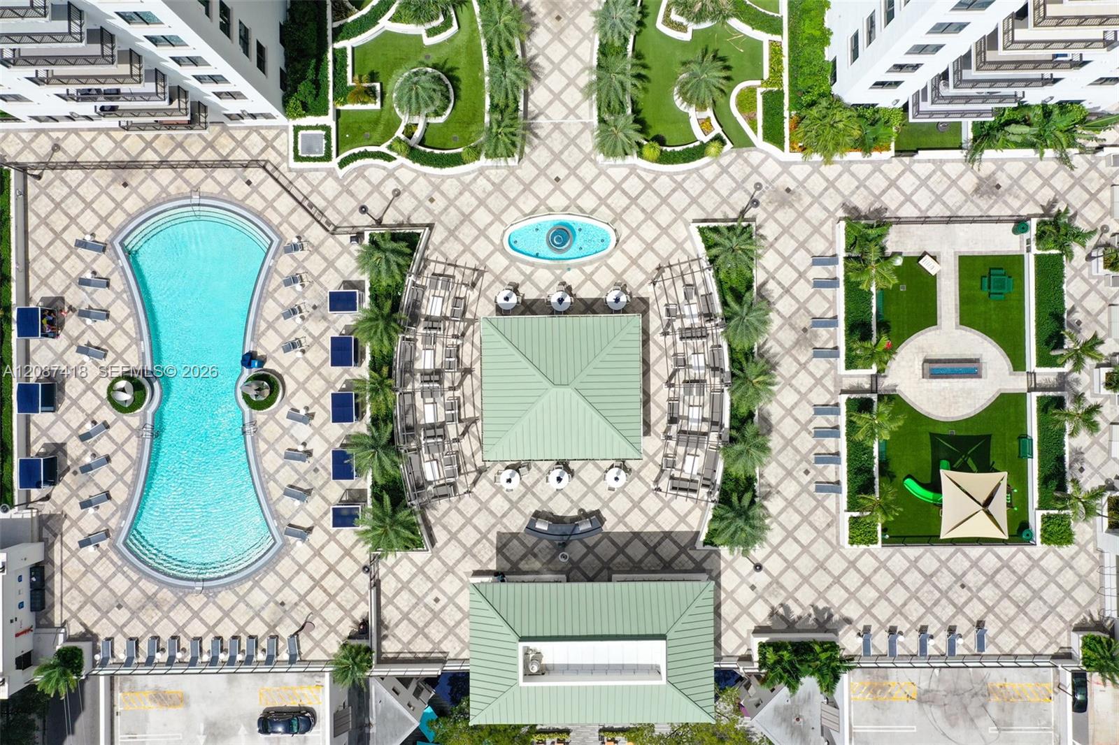 Aerial view of a condominium courtyard with a curved pool, palm-lined gardens, and patterned stone paving.