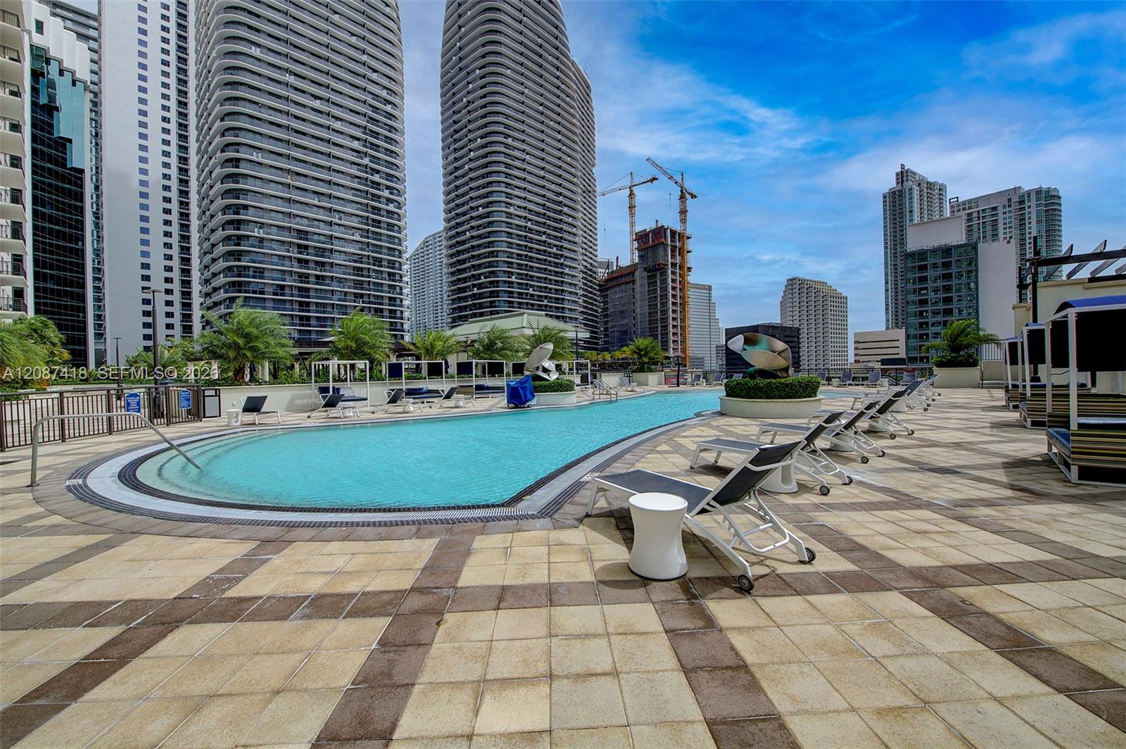 Outdoor pool and sun deck surrounded by Miami high-rises, with lounge chairs and sculptural planters.