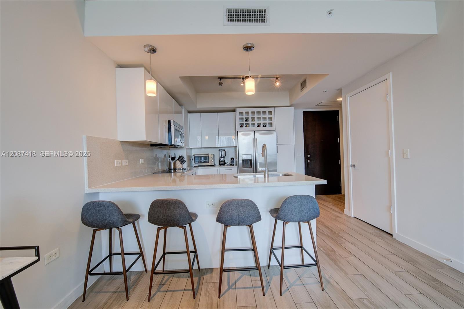 Modern condo kitchen with white cabinets, stainless appliances, and a peninsula lined with four gray stools.