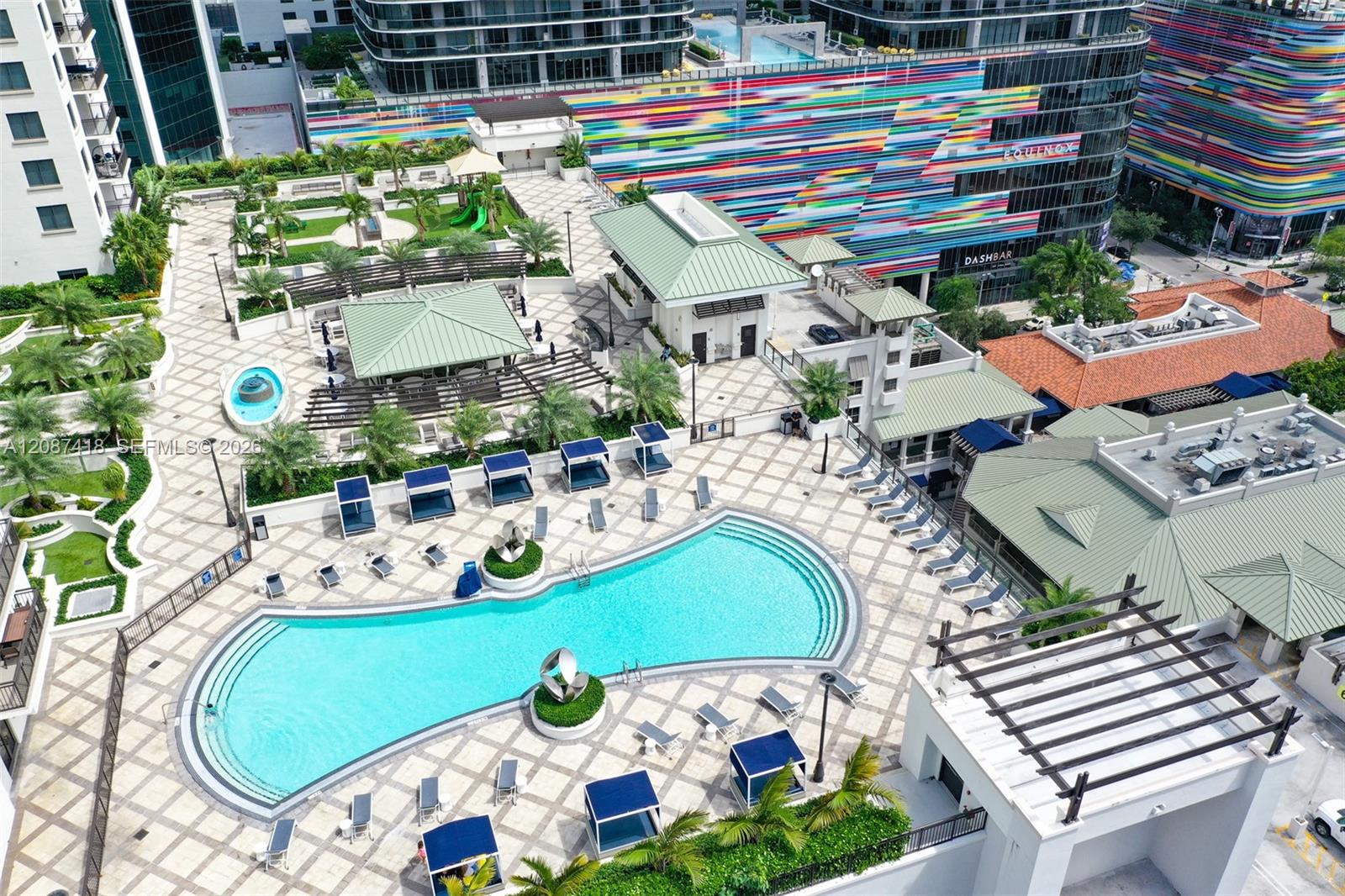 Aerial view of a rooftop pool deck with a curved pool, lounge chairs, and colorful neighboring buildings.