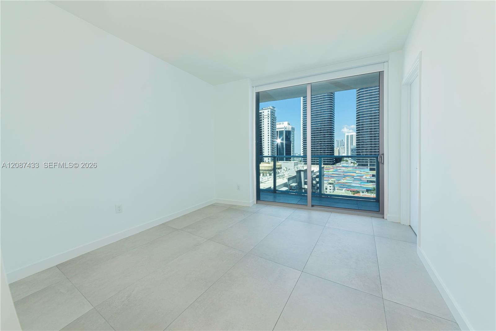 Empty tiled room with sliding glass doors and a balcony view of downtown high-rises.
