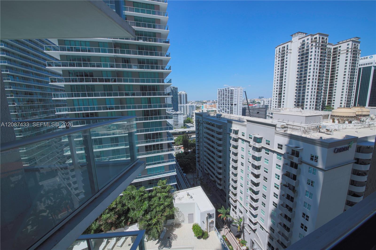 Miami high-rise city view from a balcony, with neighboring condominium towers beneath a clear blue sky.