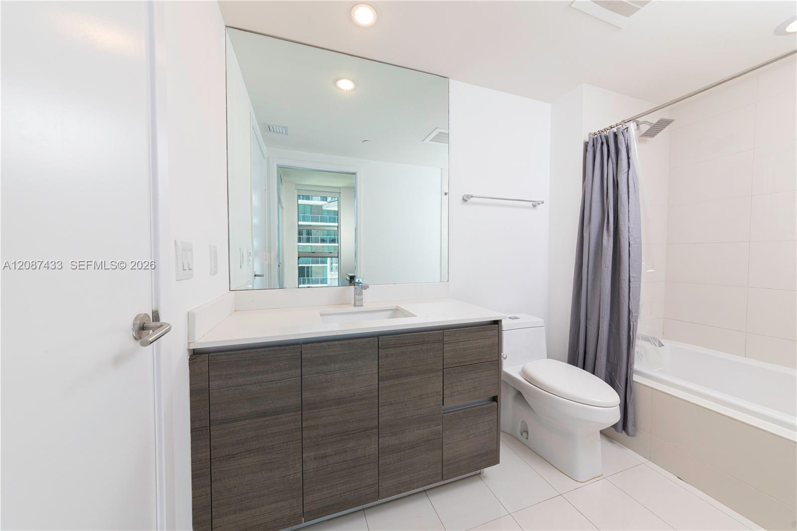 Modern bathroom with a wide dark vanity, large mirror, and tub with gray shower curtain.