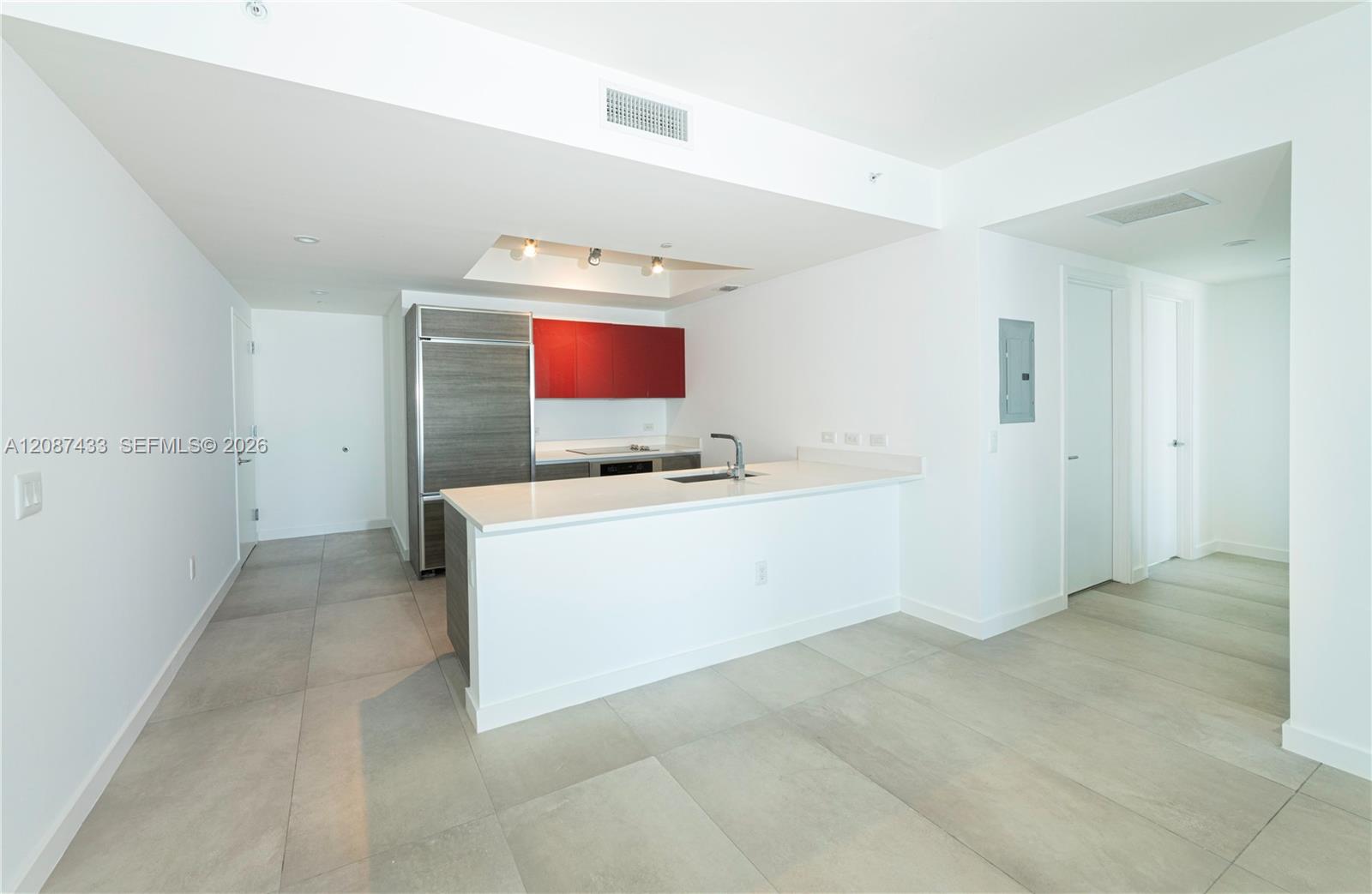 Vacant apartment kitchen with a white island, gray refrigerator, and red upper cabinets.