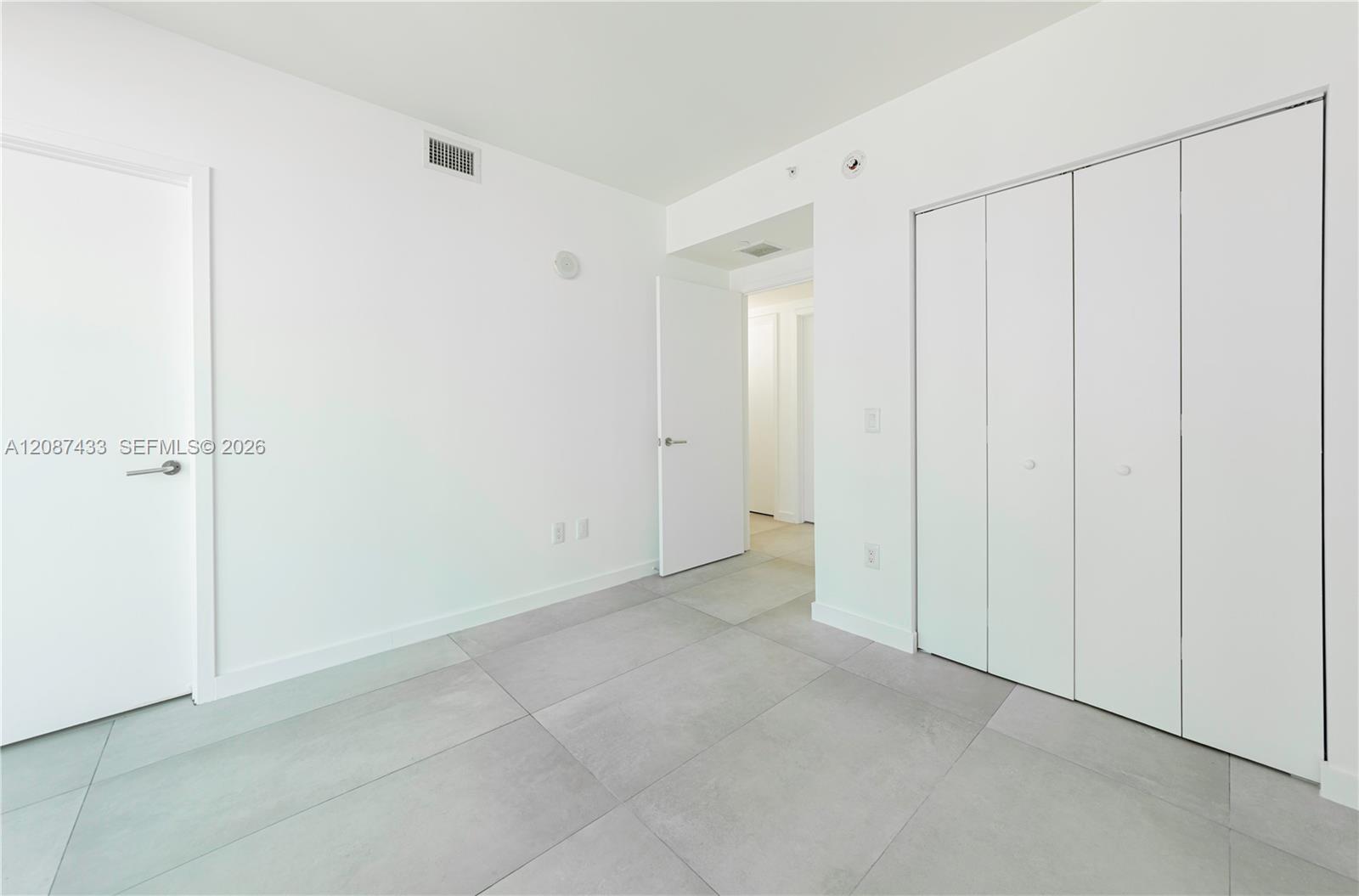 Vacant room with large gray tiles and a built-in white closet.